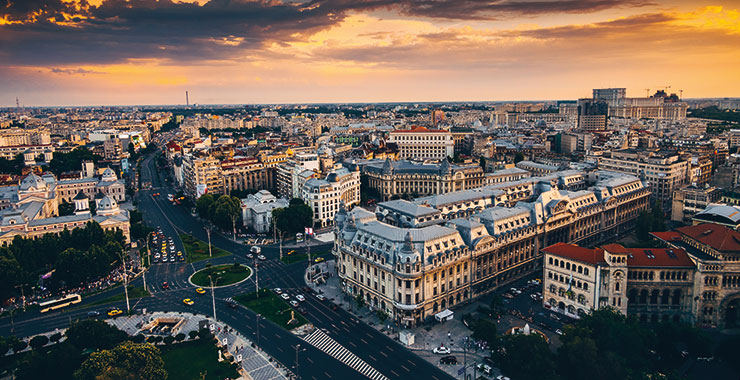 An aerial view of Bucharest, Romania, at sunset, featuring the Palace of the Parliament and the city's historic center